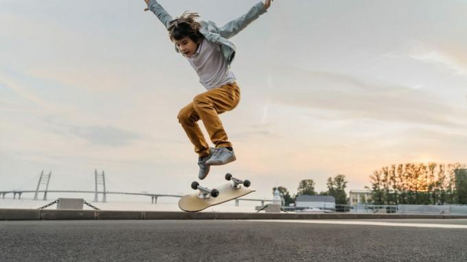 सड़क पर स्केटबोर्ड पर कूदता लड़का। सूर्यास्त के समय स्केटबोर्ड पर ओली का अभ्यास करने वाले मज़ेदार बच्चे स्केटर।
